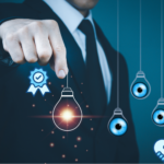 A person in a business suit is pointing at a glowing lightbulb icon, surrounded by symbolic graphics representing vision, innovation, and quality assurance.
