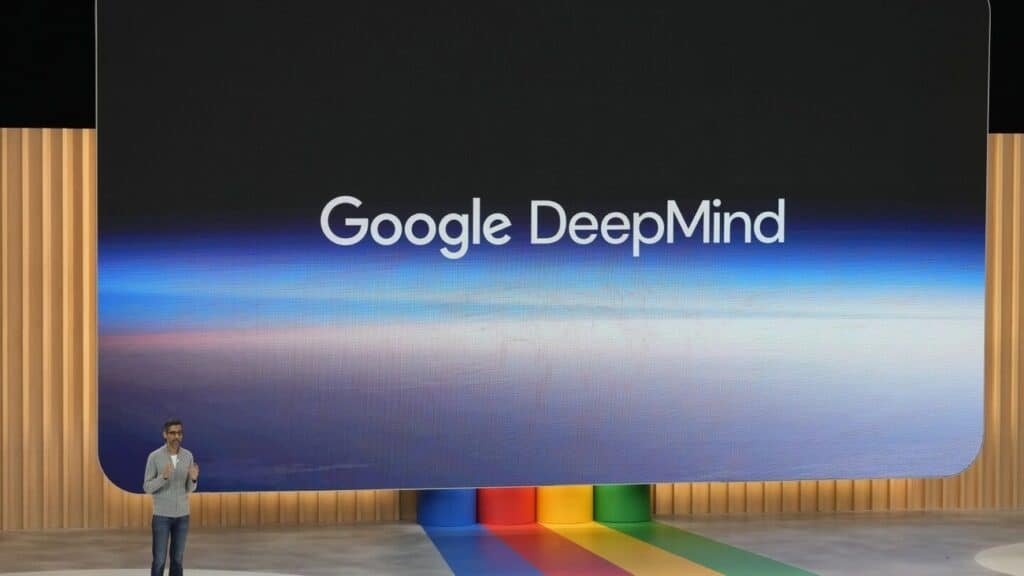 Sundar Pichai presenting on stage with Google DeepMind logo displayed on a large screen in the background.