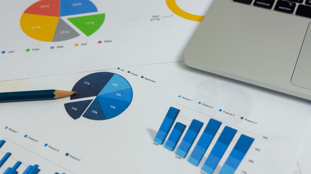 Close-up of printed business charts and graphs, including pie charts and bar graphs, with a pencil and the corner of a laptop visible.