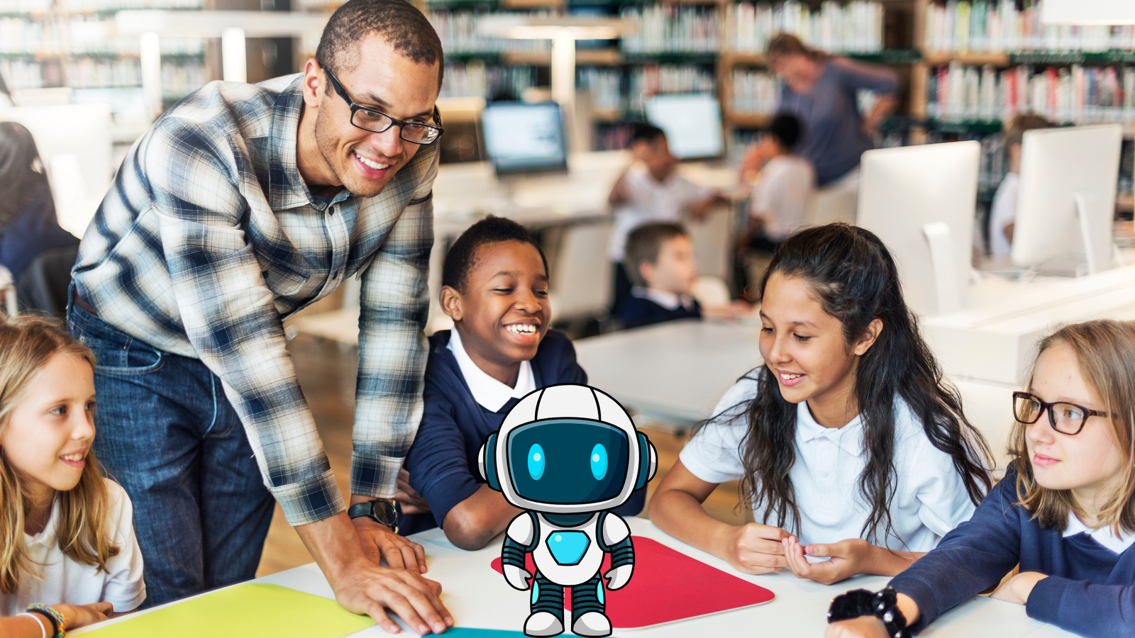 A male teacher in a plaid shirt and glasses leans over a table, smiling at three children in school uniforms, with a small cartoon robot figure placed centrally on the table. The scene is a school library or computer lab.